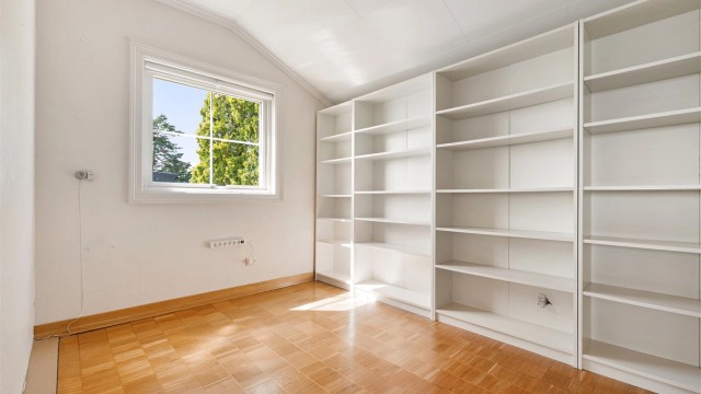 Etasjen har ett soverom med skråtak langs den ene veggen. En vegg med innebygde hyller gir gode oppbevaringsmuligheter, og vinduet vender mot hagen.