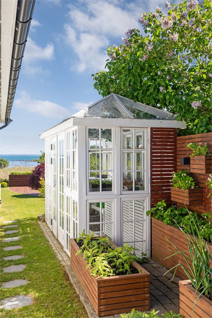 Sjarmerende, hvitmalt drivhus med sprossevinduer og glasstak -  flere plassbygde plantekasser, godt tilrettelagt for hobbygartneren. 