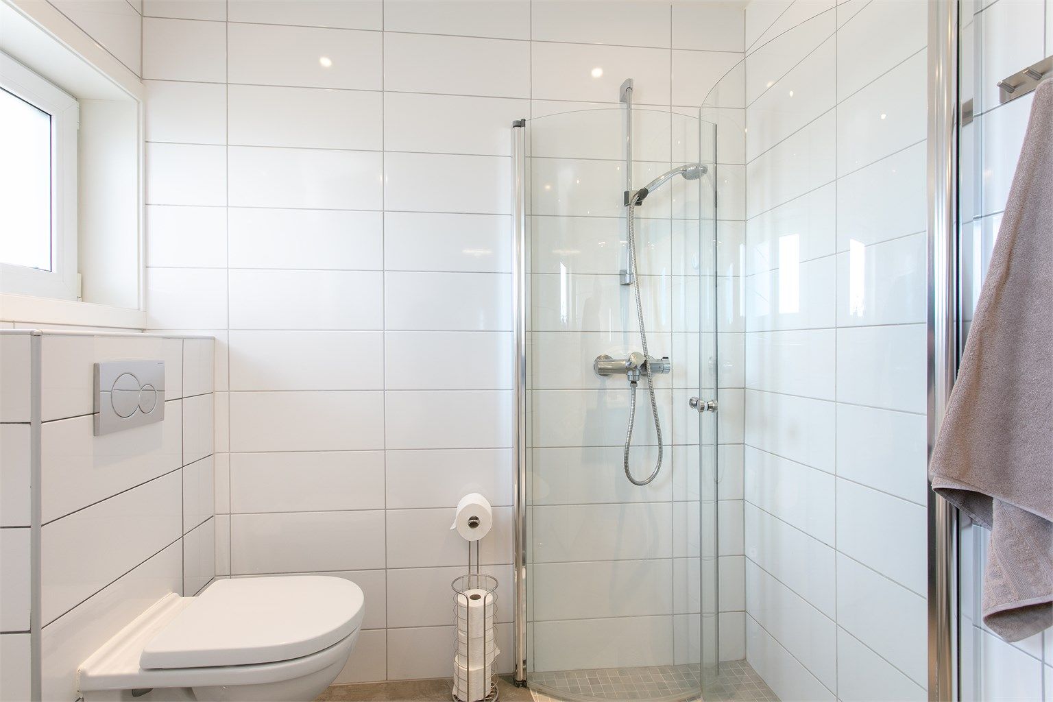 Dusjhjørne med foldbare glassvegger og vegghengt dusjarmatur. Vegghengt toalett. Elektrisk styrt vifte