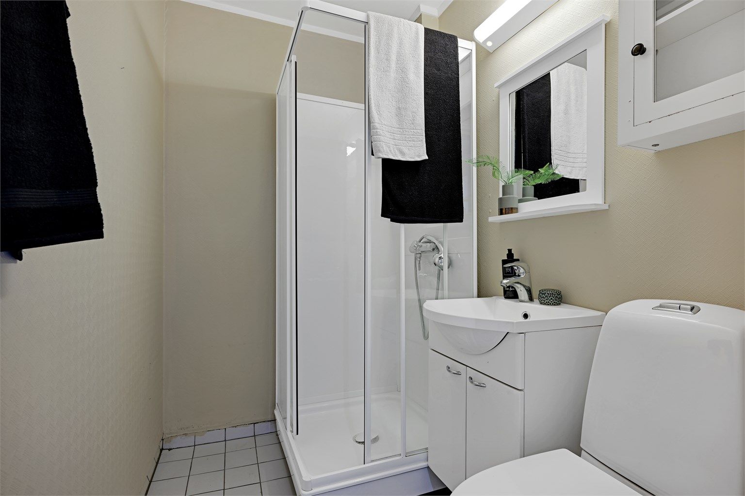 Badet er utstyrt med dusjkabinett, toalett og servant med underskap.