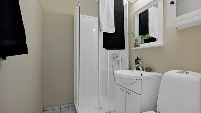 Badet er utstyrt med dusjkabinett, toalett og servant med underskap.