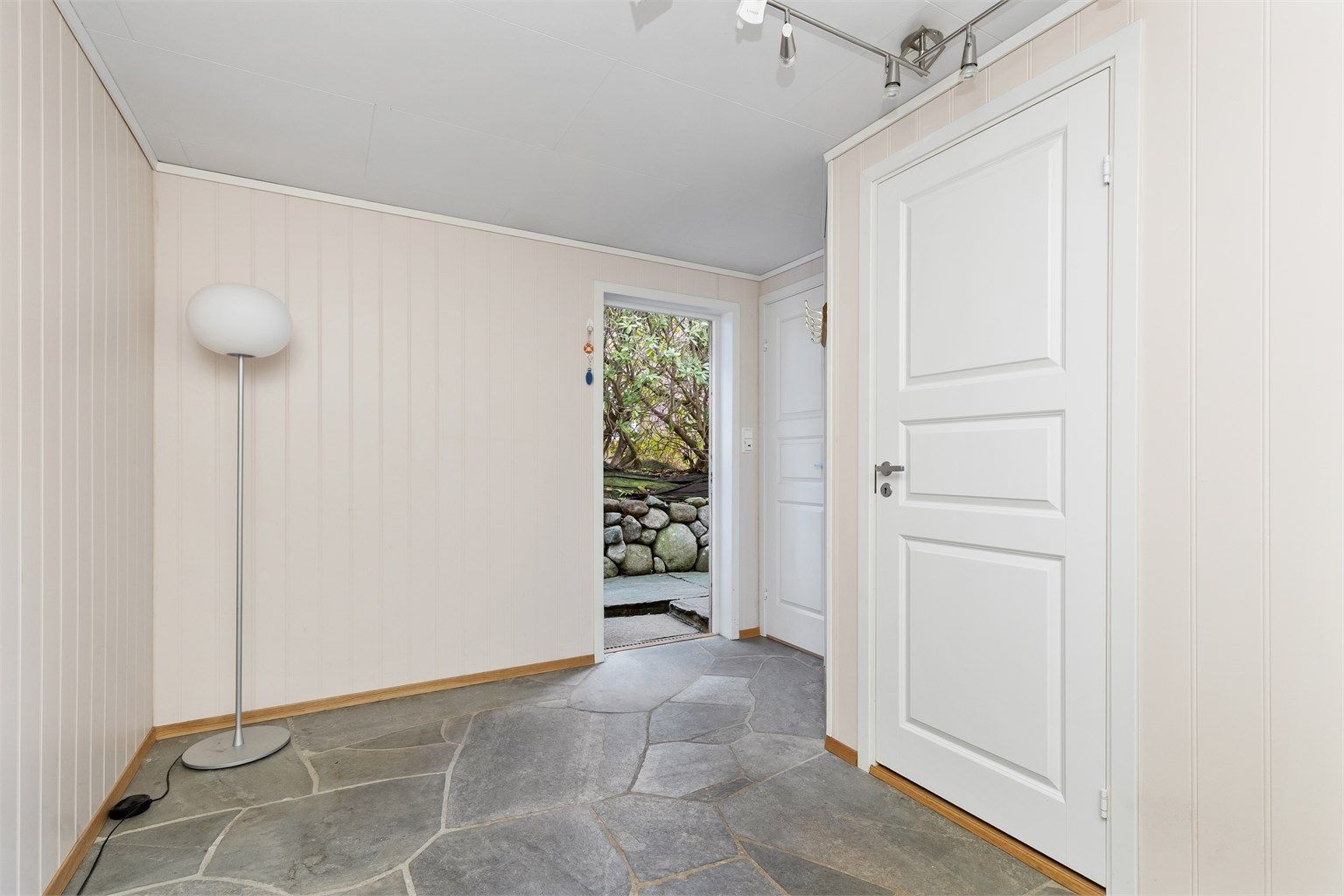 Gang i kjellerens hoveddel med skiferheller på gulv og utgangsdør til terrenget.