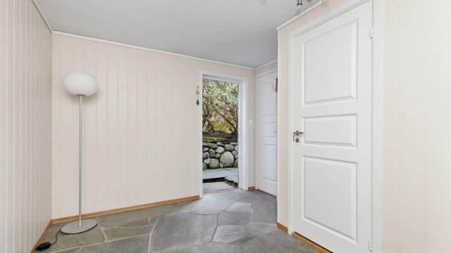 Gang i kjellerens hoveddel med skiferheller på gulv og utgangsdør til terrenget.