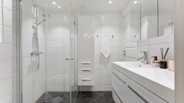 Badet har vegghengt toalett, vegghengt servantskap med dobbel nedsenket servant, vegghengt speilskap med overbelysning og dusjsone med innfellbare glassdører