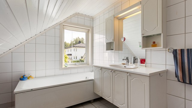 Svært funksjonelt baderom med badekar, servantinnredning, speilskap og toalett.