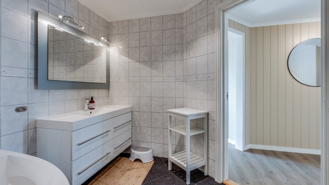 Flislagt bad i 1. etasje med stor baderomsinnrending med skuffer og speil med overlys. Hjørnebadekar og vegghengt toalett.
