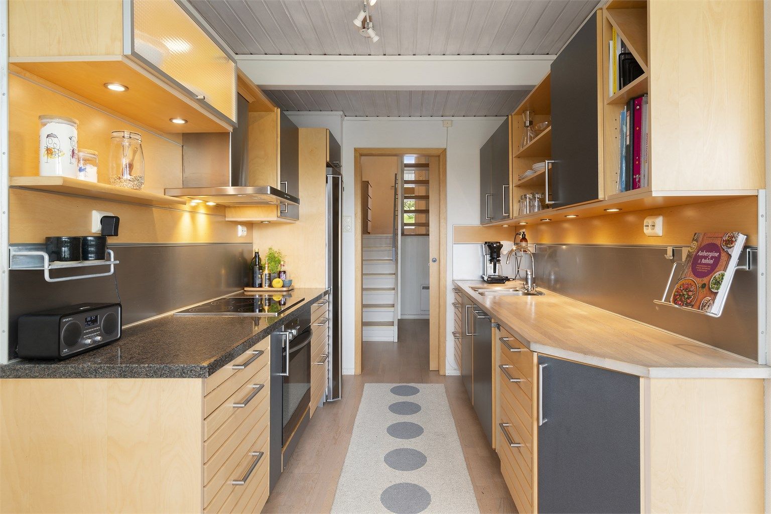 Fra entréen og ned trappen er det direkte tilkomst til kjøkkenet. Innredningen er fra HTH med benkeplate i stein og heltre. Stekeovn og oppvaskmaskin er integrert i innredningen. Platetopp og oppvaskkum nedfelt i benkeplate - frittstående kjøleskap