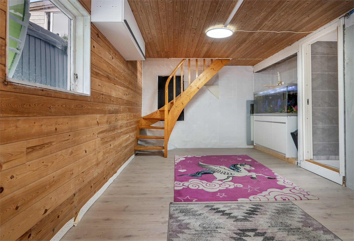 Kjellerstue med lakkert trapp og vegger med panel.