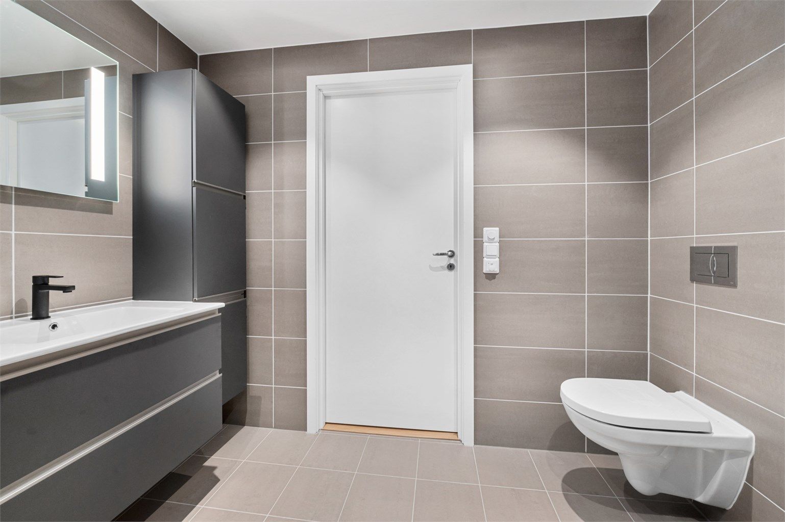 Badet måler 5 kvm og er pent flislagt med varme i gulv og lekker innredning med mørke glatte fronter. 