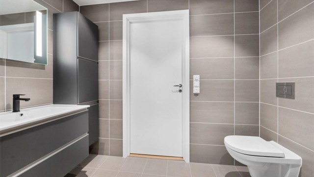 Badet måler 5 kvm og er pent flislagt med varme i gulv og lekker innredning med mørke glatte fronter.