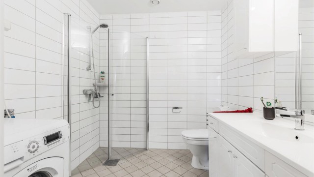 Hybel : Baderom fra byggeår. Flislagt gulv med gulvvarme. Flislagte vegger. Vegghengt servantinnredning. Speilskap med overlys. Dusjhjørne med dører. Vegghengt dusjarmatur. Gulvstående toalett.