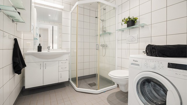 Baderommet har dusjhjørne med skyvedørsramme og opplegg for vaskemaskin.