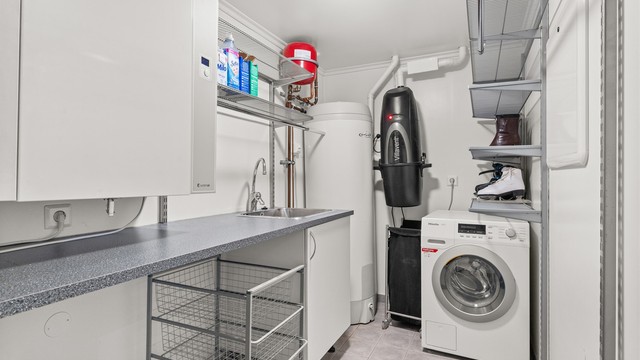 Praktisk vaskerom med flislagt gulv med gulvvarme. Boligens tekniske installasjoner er samlet her, inkludert bl.a. aggregat for balansert ventilasjon og sentralstøvsuger