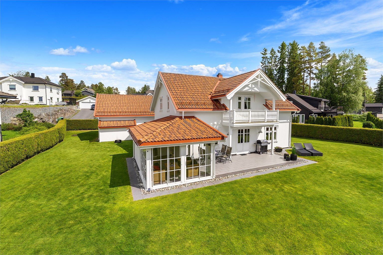 Tomten er pent opparbeidet med en stor, flat plen og hekk som rammer inn eiendommen.