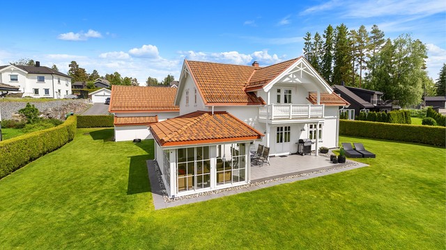 Tomten er pent opparbeidet med en stor, flat plen og hekk som rammer inn eiendommen.