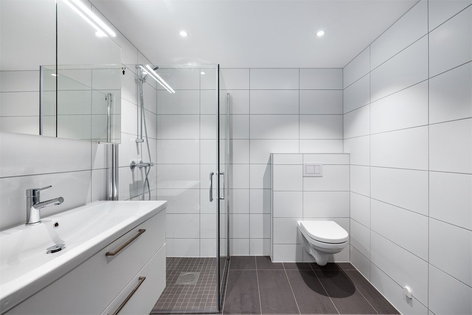 Badet er levert av kvalitetsleverandøren Sigdal og har behagelig gulvvarme. Innredningen er stilren med vegghengt toalett, dusjhjørne med glassdører og et romslig servantskap.