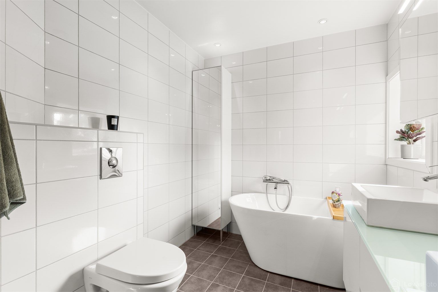 I tillegg til dusj har badet et frittstående badekar og vegghengt toalett. Downlights gir god belysning.