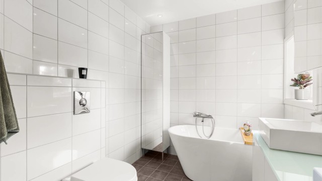 I tillegg til dusj har badet et frittstående badekar og vegghengt toalett. Downlights gir god belysning.