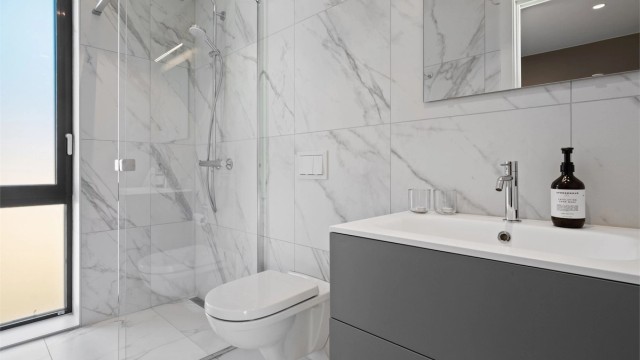 Badet har flislagte gulv og vegger, innredet med servant, vegghengt toalett og dusjhjørne.