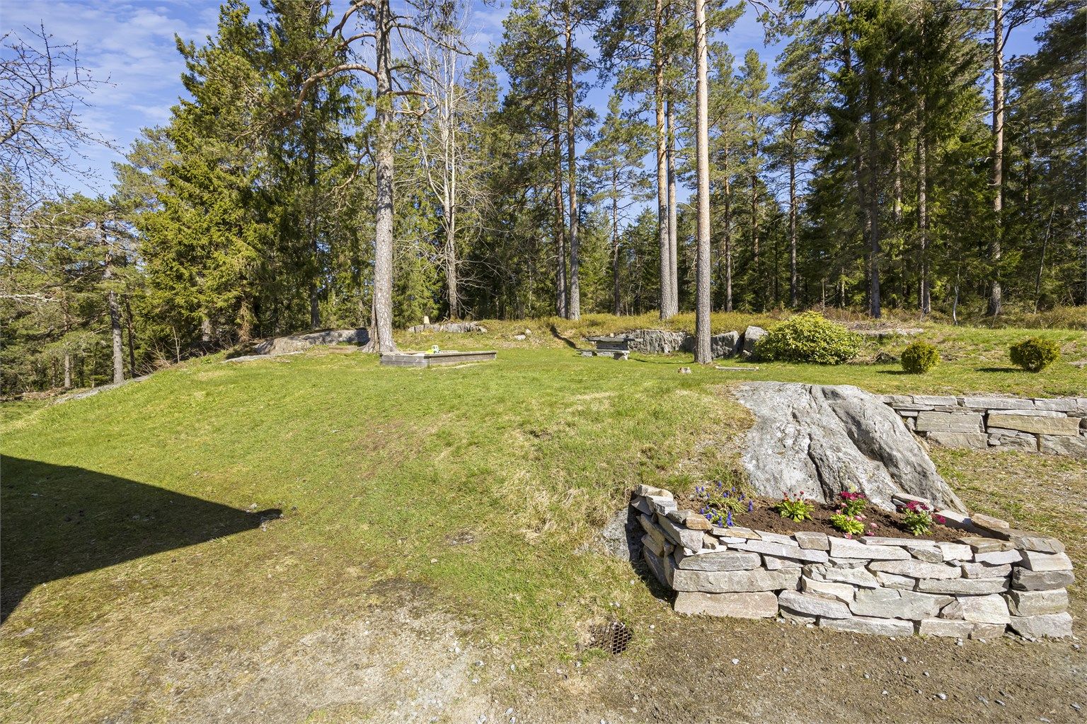 Tomten er pent opparbeidet med natursteinsmurer som skaper fine overganger i terrenget.