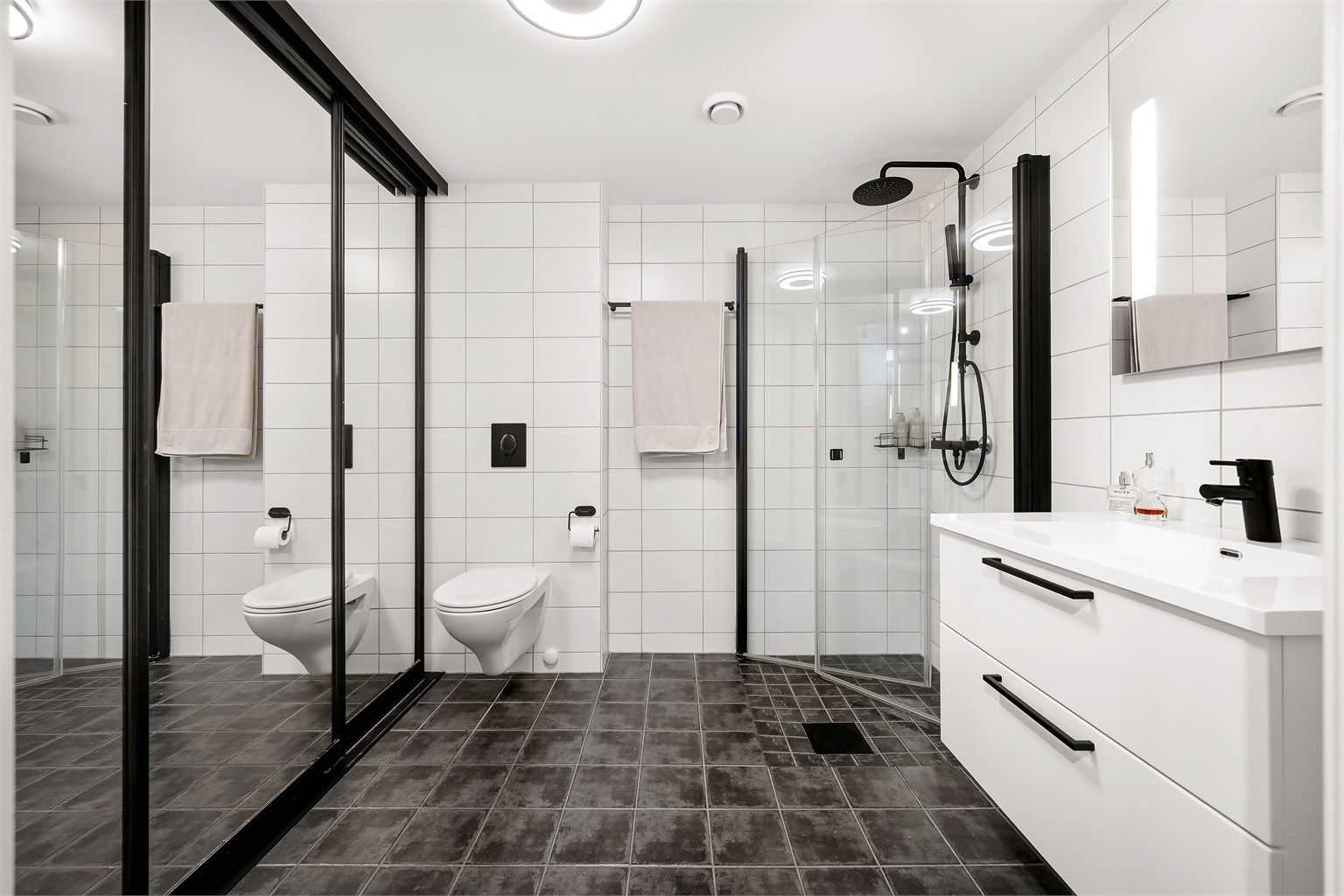 Badet har flislagt gulv med varmekabler, vegghengt toalett og dusj med innfellbare glassdører.