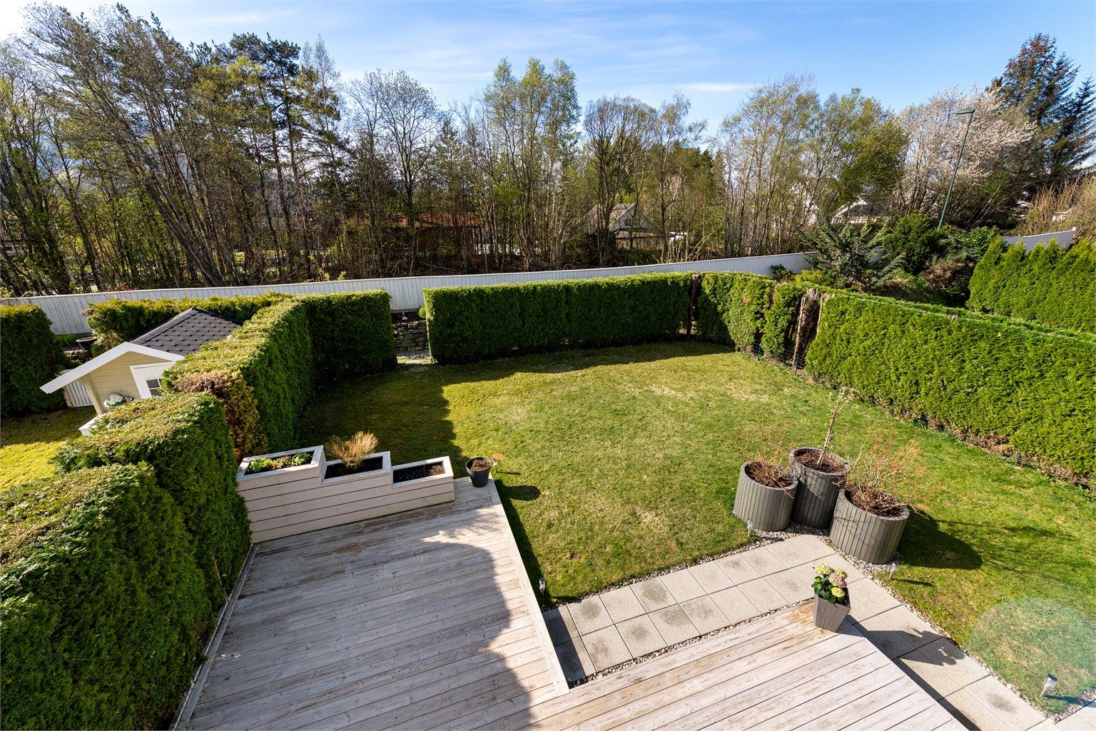 Den store hagen er pent opparbeidet med plen og omkranset av hekk, som skaper en privat og lun uteplass.