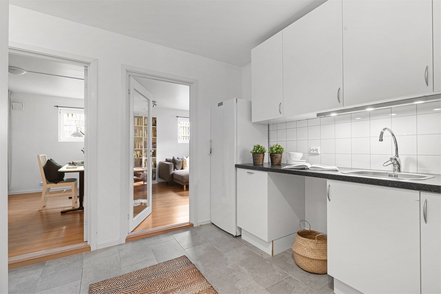 Kjøkken i underetasjen er fra 2008 og innredningen er i tidløst hvitt, med grå benkeplate. Det er plater på vegg over benk samt lys under overskap. Det er plass til å sette inn både oppvaskmaskin samt komfyr.
Varmekabler i gulv