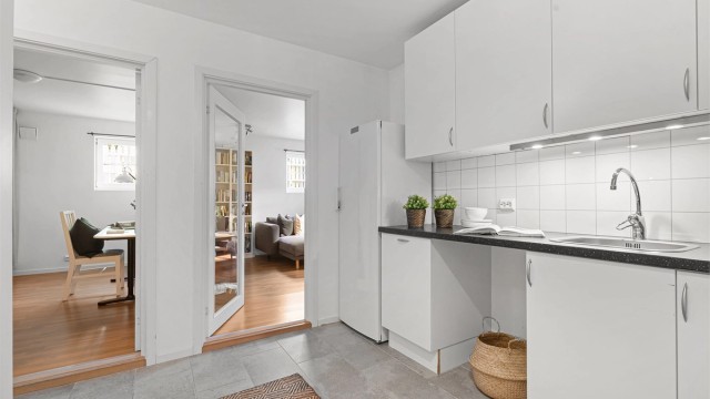 Kjøkken i underetasjen er fra 2008 og innredningen er i tidløst hvitt, med grå benkeplate. Det er plater på vegg over benk samt lys under overskap. Det er plass til å sette inn både oppvaskmaskin samt komfyr.
Varmekabler i gulv