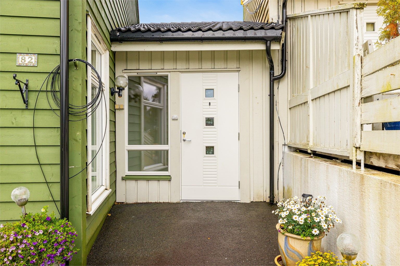 Skjermet inngangsparti med hvit ytterdør og glassfelt.
