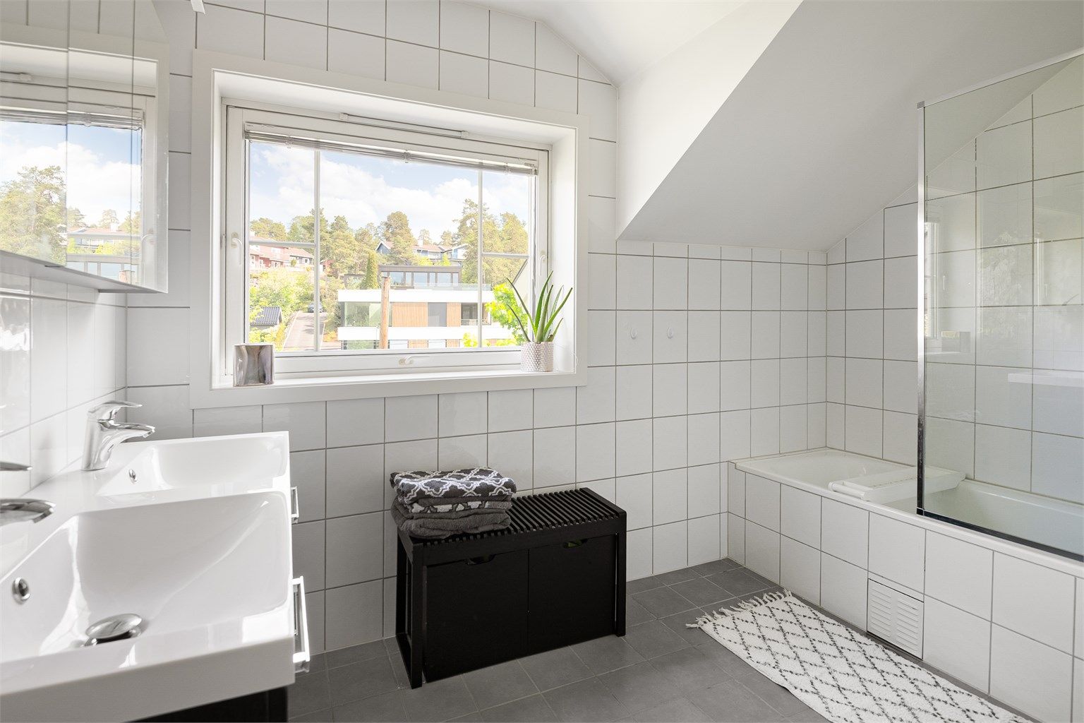 Badet er utstyrt med både badekar og dusjhjørne, samt en innredning med doble servanter.