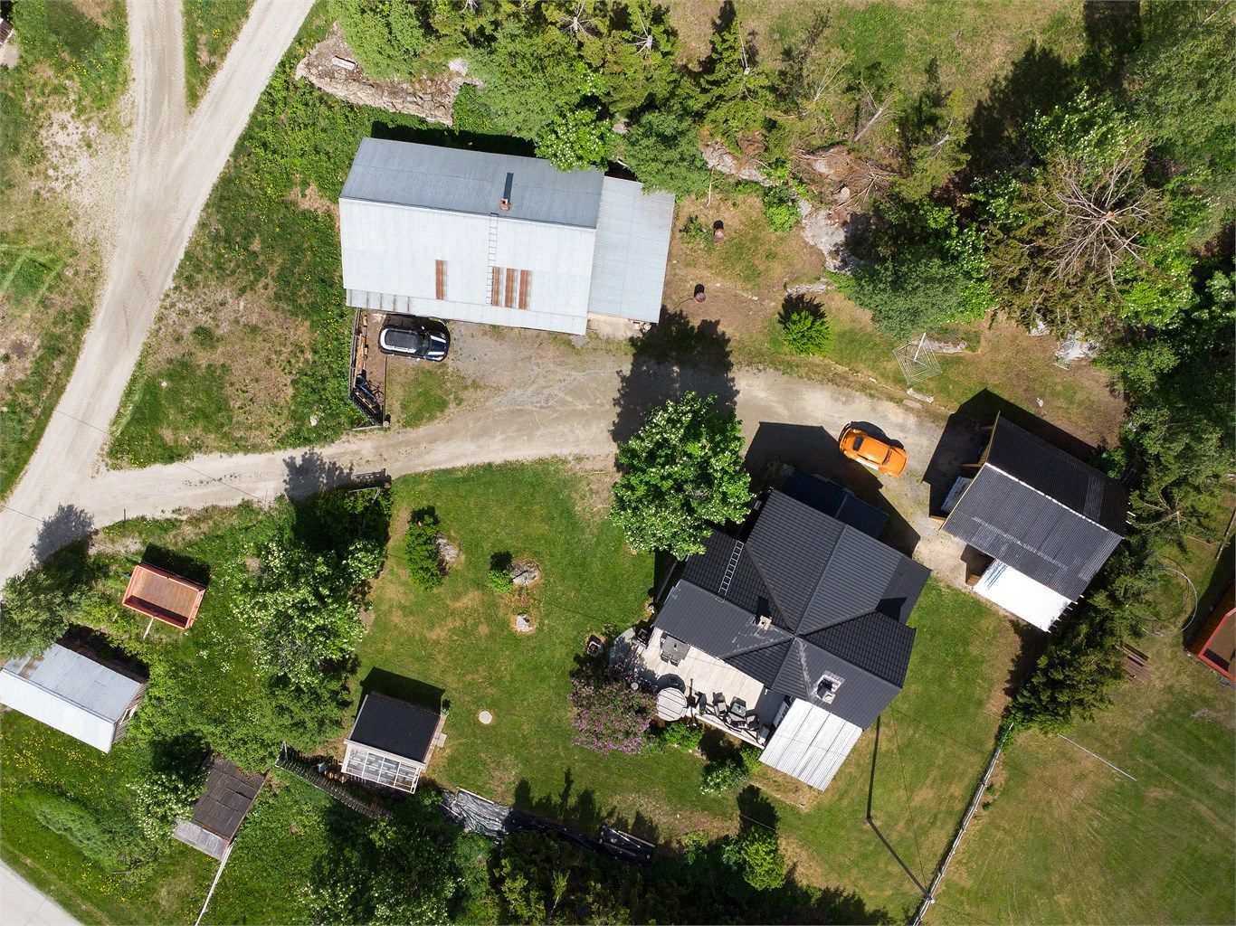 Oversikt over eiendommen med fritidsbolig, garasje, carport og drivhus.