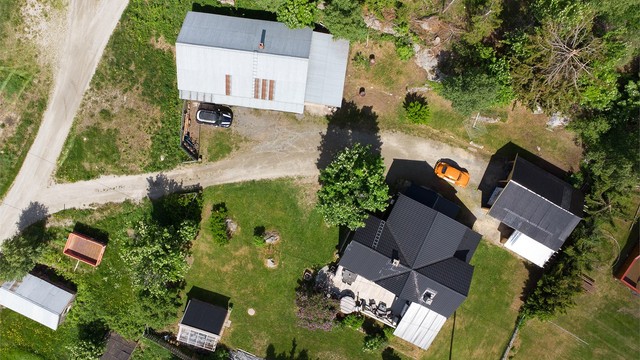 Oversikt over eiendommen med fritidsbolig, garasje, carport og drivhus.