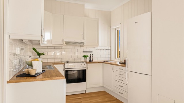 Lys og pen kjøkkeninnredning. Det er montert hvite, profilerte fronter og benkeplater i laminat. Det er montert flis mellom overskap og benkeplate.