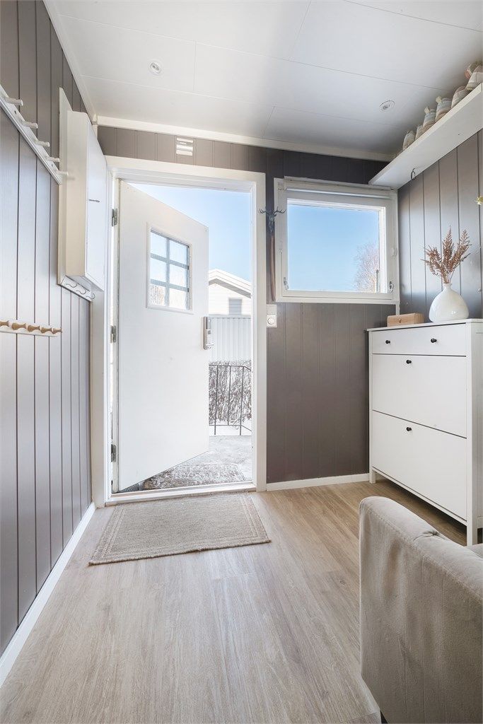 Man kommer inn i en lys entré med laminat på gulv og malt panel på veggene