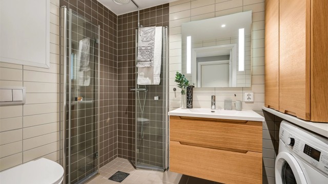 Det er innredet med en delikat servant med skuffer under, spotter i taket, toalett og dusjhjørne med innfellbare glassdører.