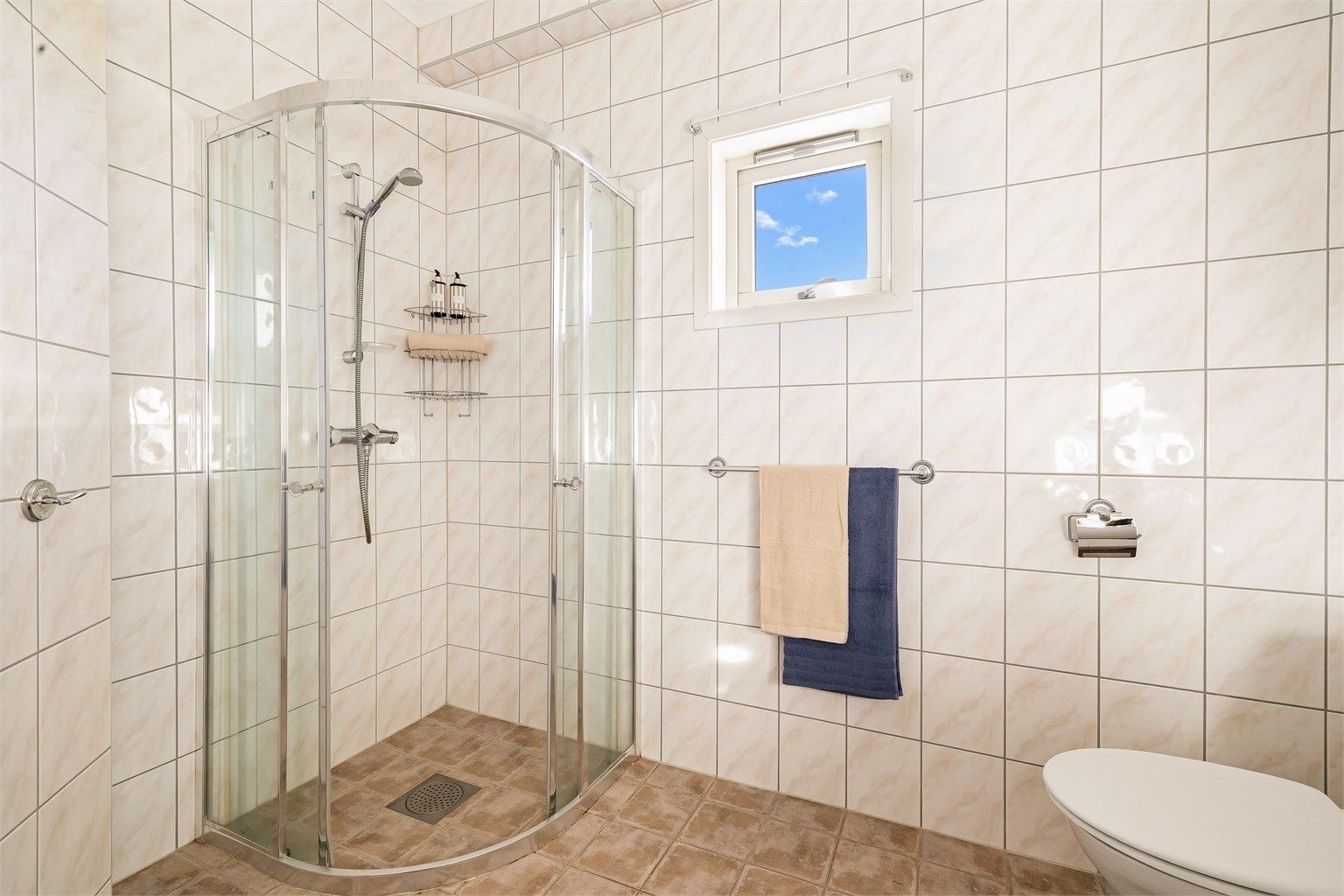 Det er montert lys innredning med profilerte fronter og heldekkende servant. Over servanten er det montert speil, to veggskap og lysarmatur. I tillegg er det montert et ekstra veggskap. Badet har gulvmontert toalett og dusjhjørne med dusjvegger i glass.