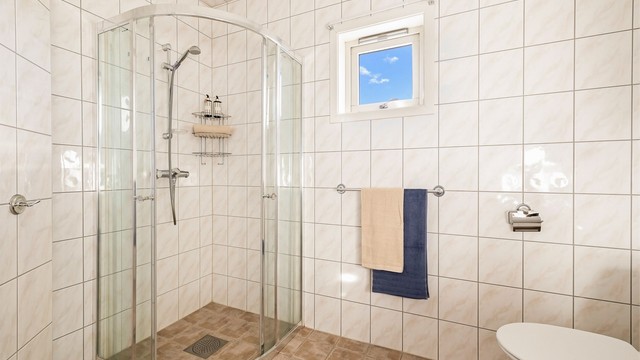 Det er montert lys innredning med profilerte fronter og heldekkende servant. Over servanten er det montert speil, to veggskap og lysarmatur. I tillegg er det montert et ekstra veggskap. Badet har gulvmontert toalett og dusjhjørne med dusjvegger i glass.