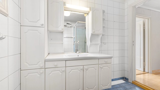 Badet er innredet med vegghengt servantinnredning med ovenpåliggende servant og armatur, speil med overlys samt dusjkabinett med dusjarmatur. Ventilasjon skjer via naturlig avtrekksventil i vegg.