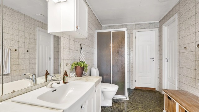Badet er innredet med fliser på både gulv og vegger. Gulvvarme og folierte himlingsplater. Vegghengt servantinnredning med overskap og to servanter. Dusjnisje med skyvedører og badekar