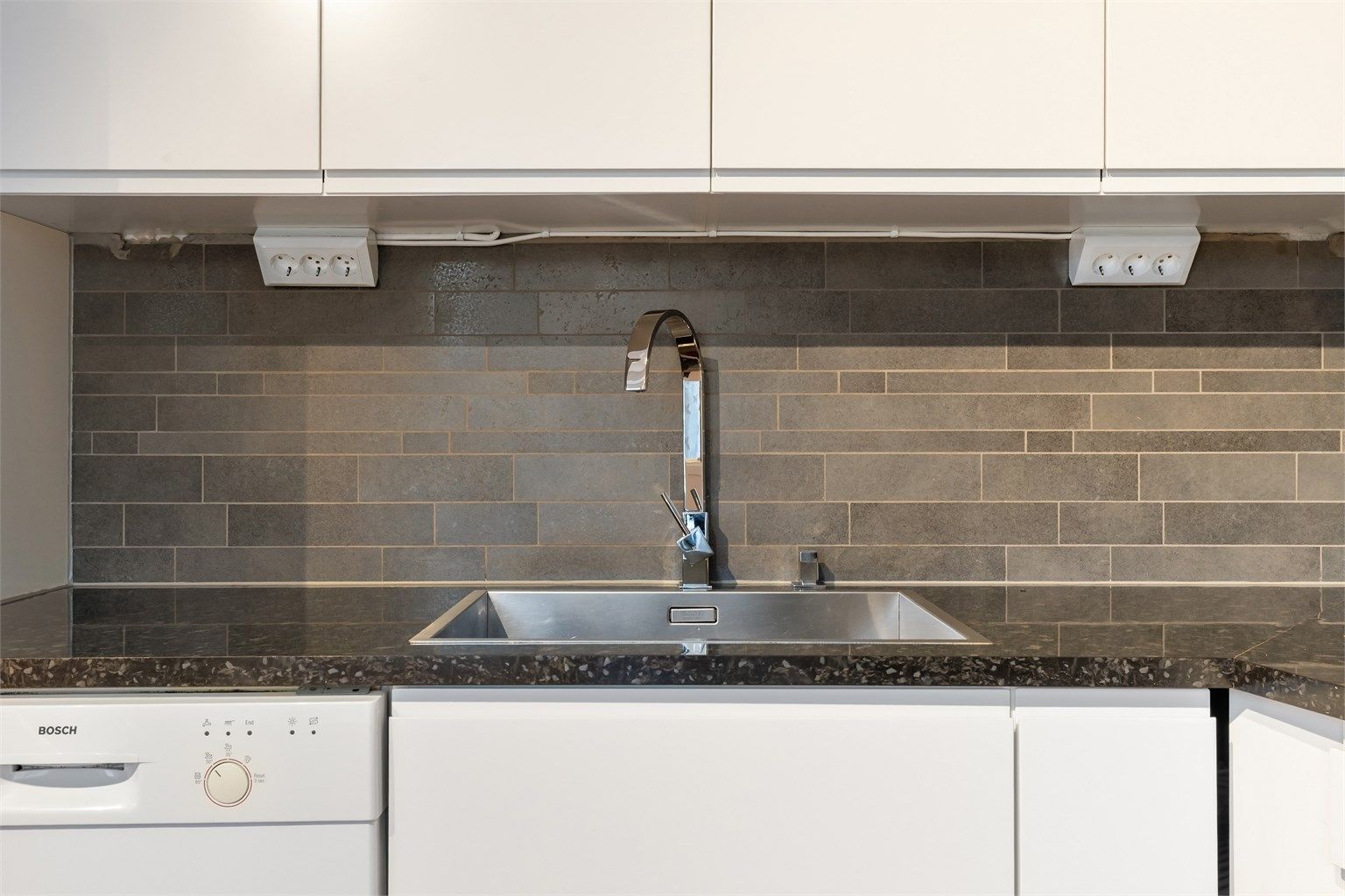 Benkeplate med nedfelt oppvaskkum, ett-greps armatur og stilrene fliser på veggen over.