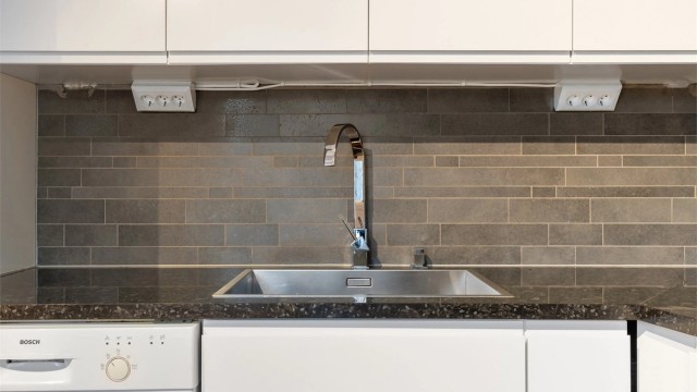 Benkeplate med nedfelt oppvaskkum, ett-greps armatur og stilrene fliser på veggen over.