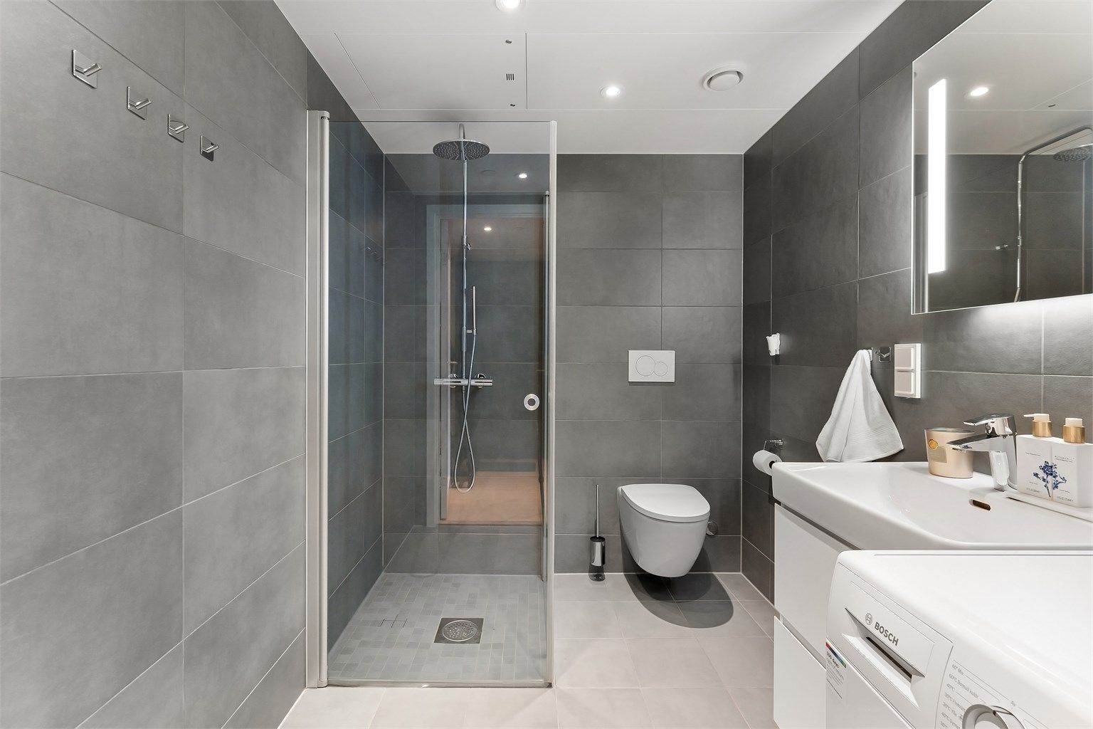 Badet holder en gjennomført standard med flislagt gulv med gulvvarme. flislagte vegger og nedsenket himling med downlights