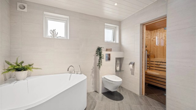 Badet gir en god romfølelse med delikate fargevalg og er innredet med vegghengt toalett, badekar og dusjnisje. De små vinduene gir godt med naturlig lys uten innsyn.