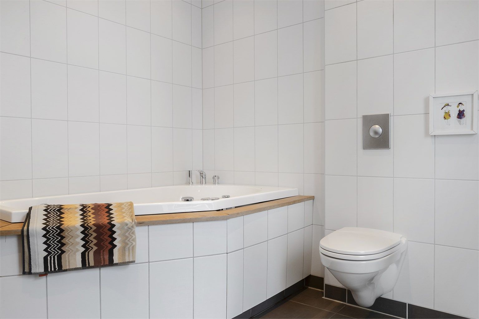 Badet er utstyrt med innbygget badekar og veggmontert toalett.