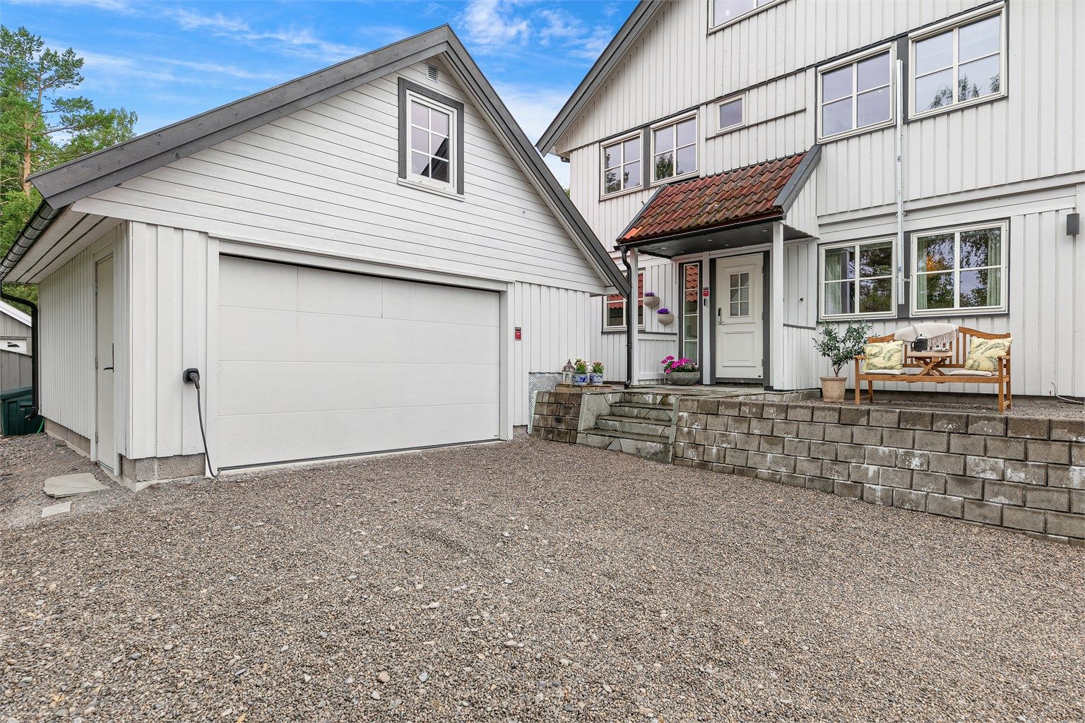 Boligens fasade sett fra gårdsplassen. Dobbelgarasje med elbillader og hyggelig inngangsparti.
