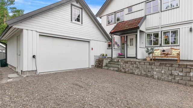 Boligens fasade sett fra gårdsplassen. Dobbelgarasje med elbillader og hyggelig inngangsparti.