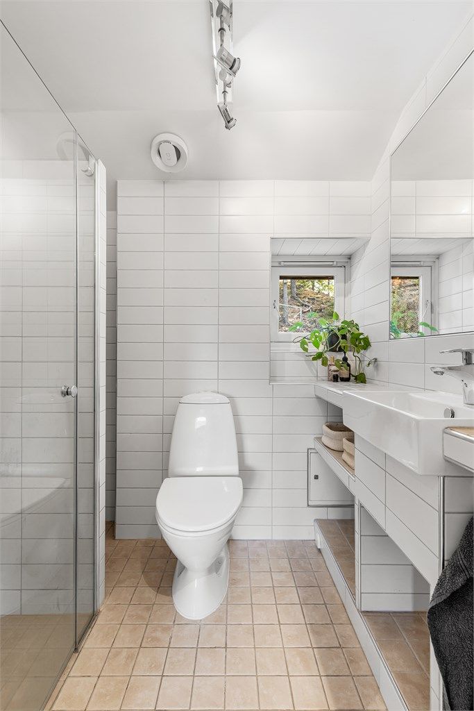 Baderommet har plassbygd og flislagt servantinnredning og gulvstående toalett, samt dusjhjørne med dører.