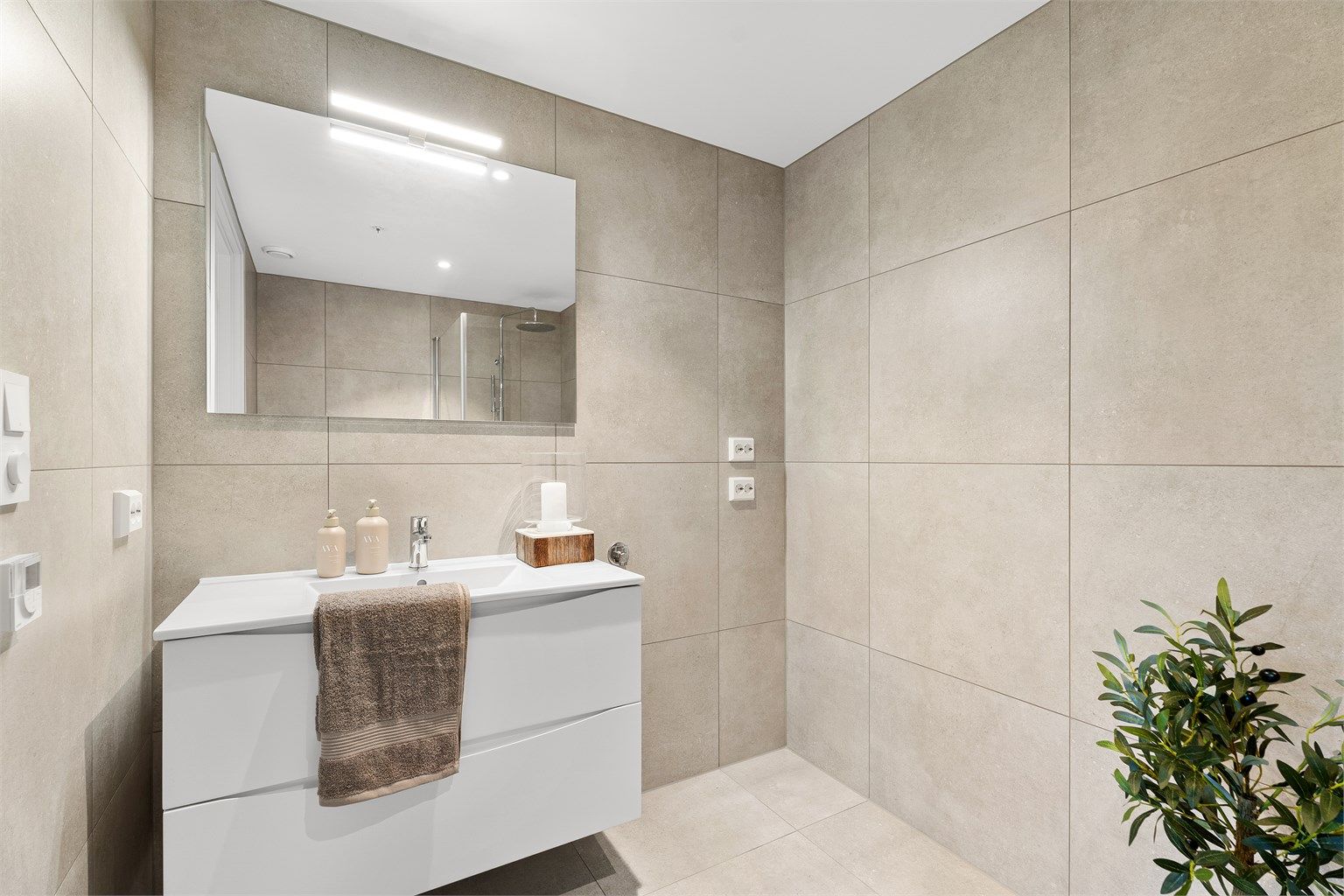 Badet har 60x60 fliser på gulv og vegger, opplegg til vaskemaskin og tørketrommel samt en større servant med oppbevaring. 