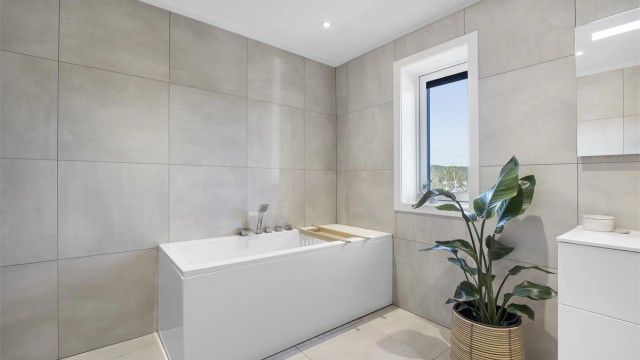 Badet i første etasje er fra byggeår, med flislagte overflater, vannbåren gulvvarme og badekar.