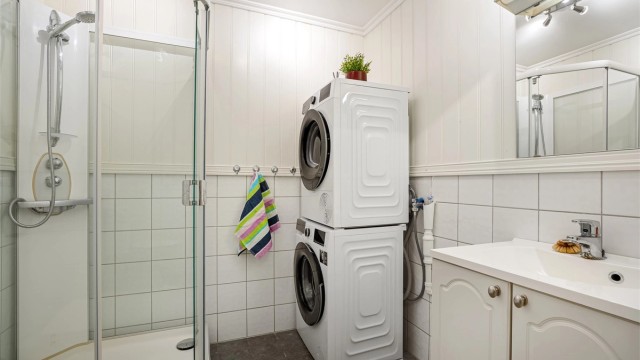 Baderom med delvis flislagte overflater og panel på øvrige flater. Det er varmekabler i gulvet som sørger for en behagelig oppvarming. Servant med skapinnredning, dusjkabinett, toalett og opplegg til vaskemaskin.
